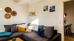 Ein modernes Wohnzimmer mit einem grauen Ecksofa, einem Holztisch und einer Pendelleuchte.