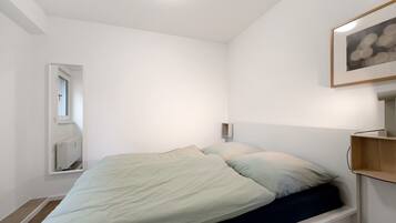 A bedroom with a bed, a window, a radiator, and a framed picture on the wall.