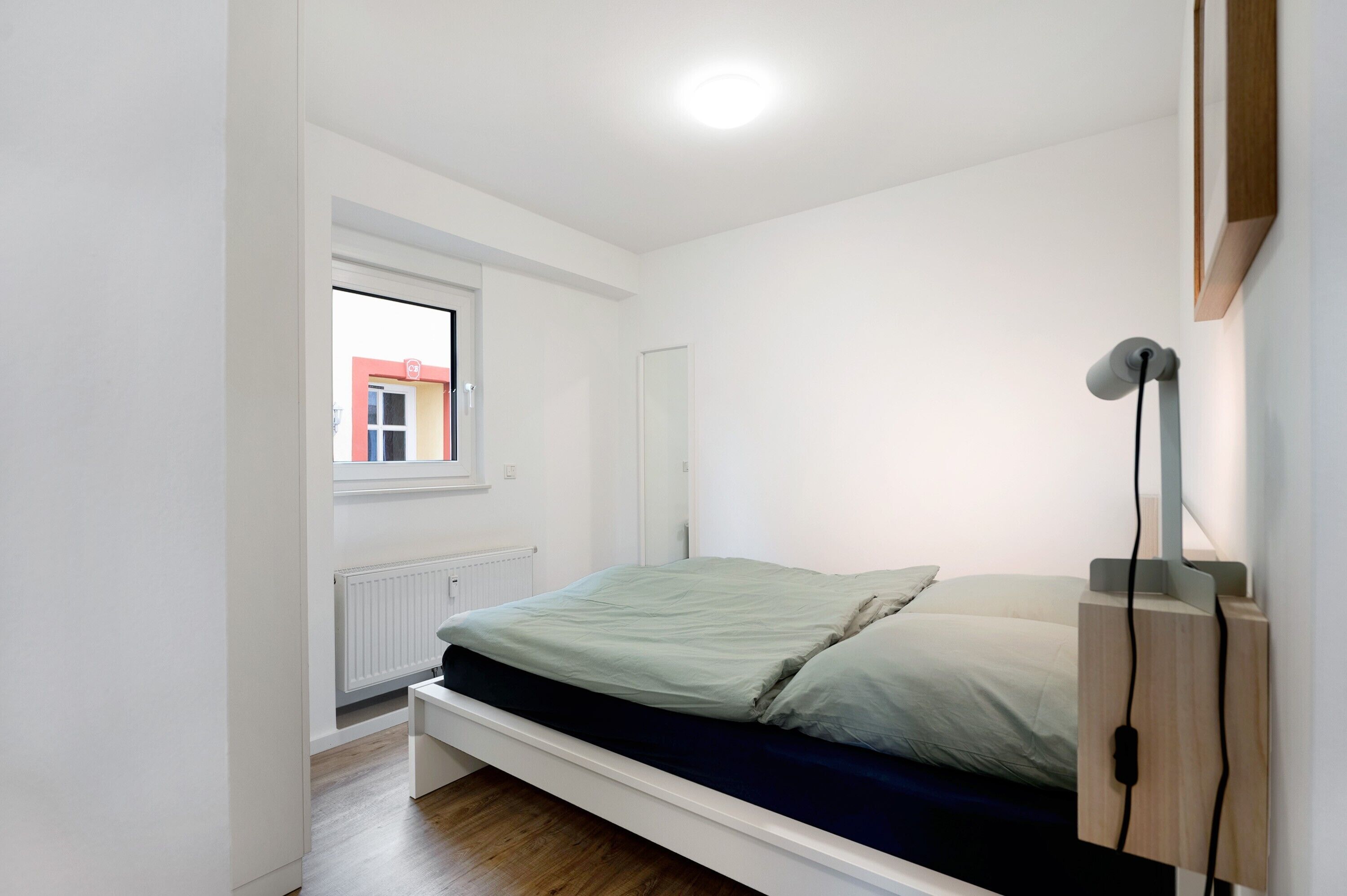 Une petite pièce lumineuse, avec un lit simple, une fenêtre et un radiateur.