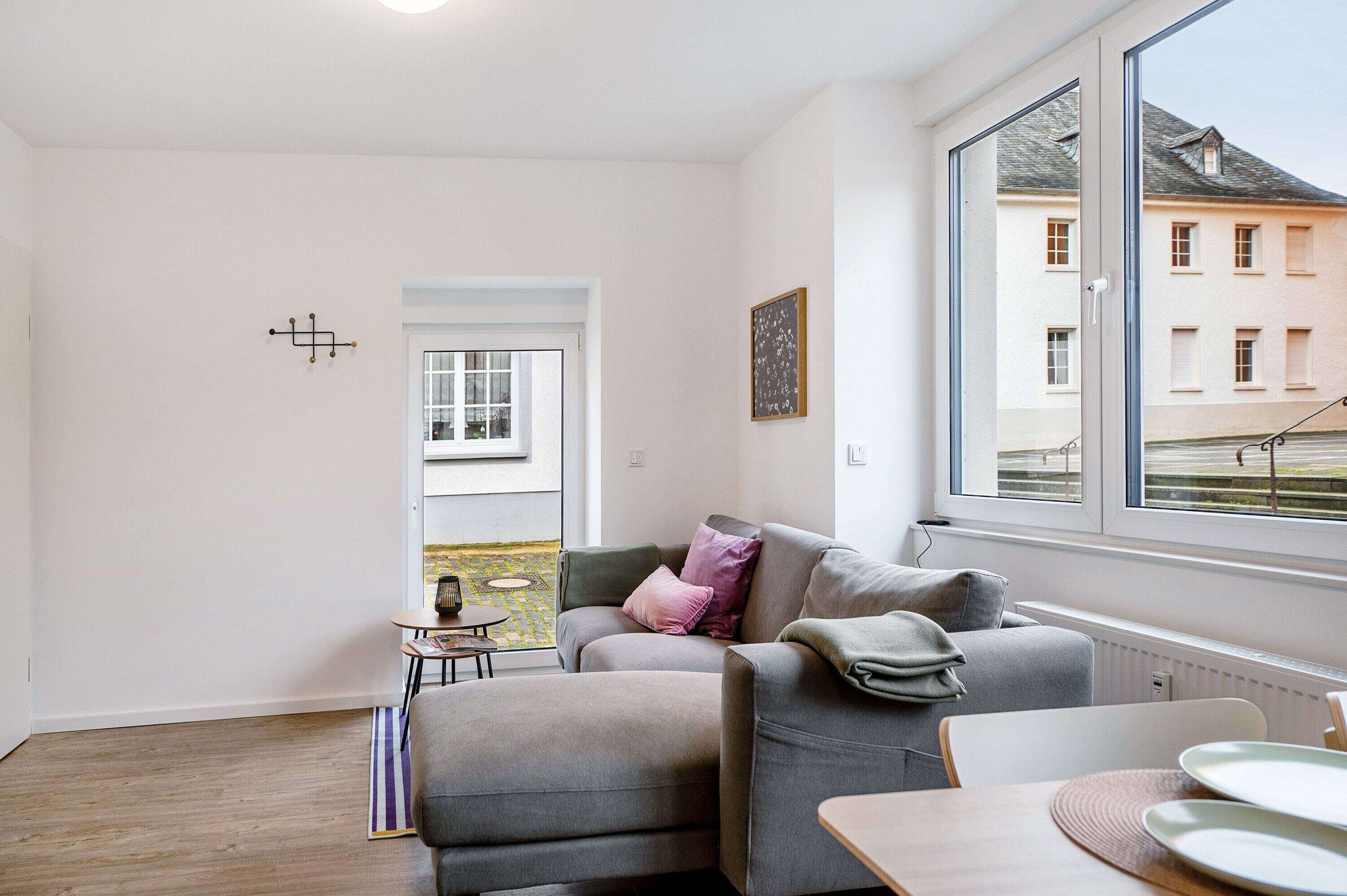 Un salon moderne avec un canapé gris, une petite table et une vue sur un immeuble par une grande fenêtre.