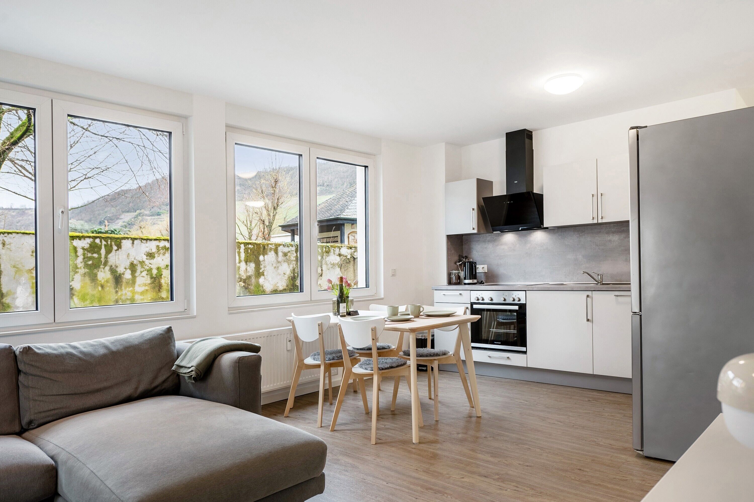 A modern kitchen with a dining area, large windows, and a sofa.