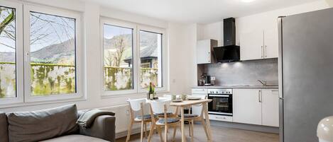 A modern kitchen with a dining area, large windows, and a sofa.