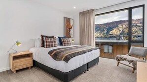 Ein Schlafzimmer mit einem großen Bett, einem Nachttisch, einem Sessel und Bergblick durch ein Fenster.