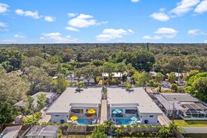A residential area with a large house featuring a swimming pool, multiple umbrellas, and a view of a forested landscape.