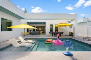 A modern outdoor pool area with lounge chairs, yellow umbrellas, and inflatable toys.