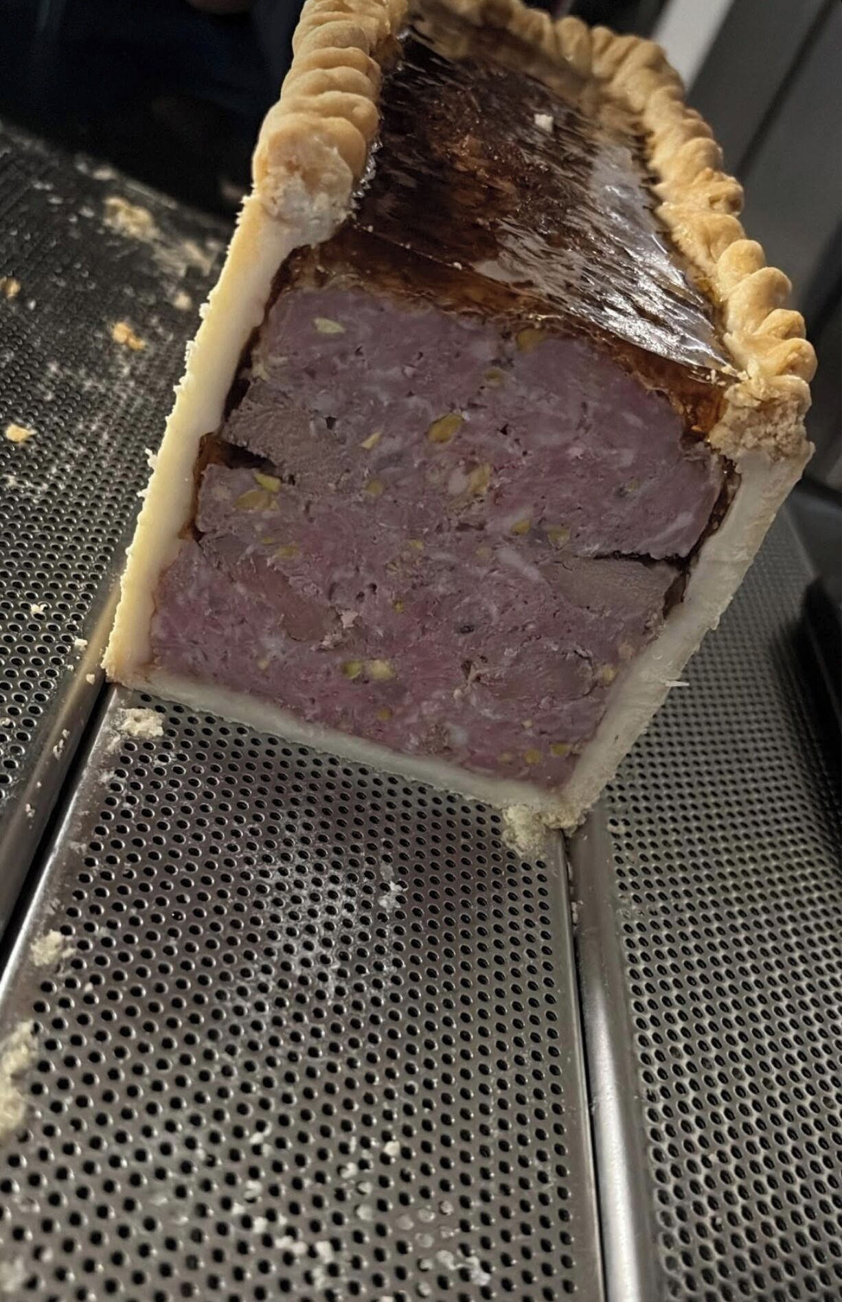A close-up of a meat pie with a crust, placed on a perforated metal surface.