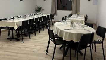 A dining area with multiple round tables set for a meal, featuring black chairs and white tablecloths.
