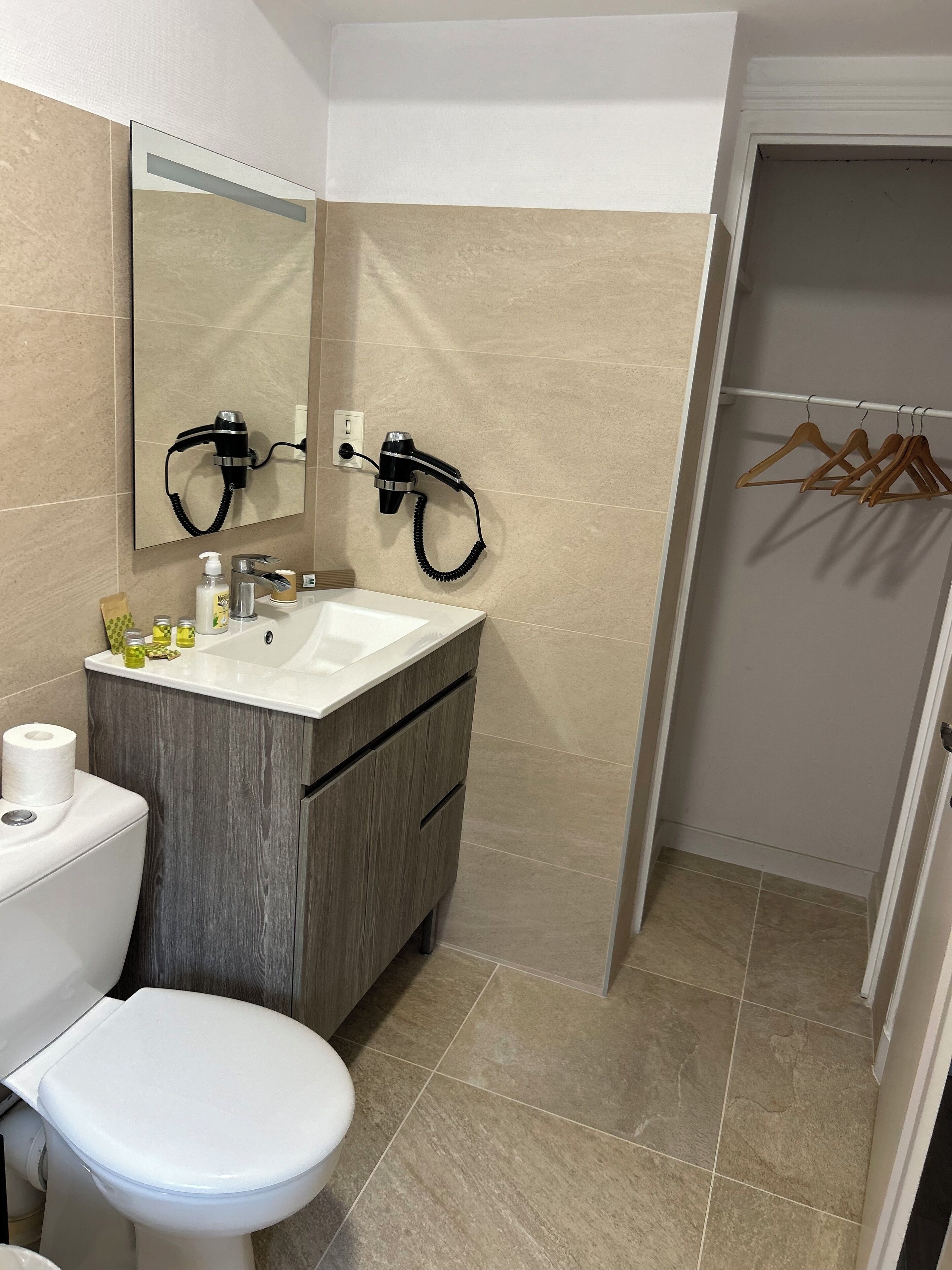 Un baño con inodoro, lavamanos y secador de pelo montado en la pared.