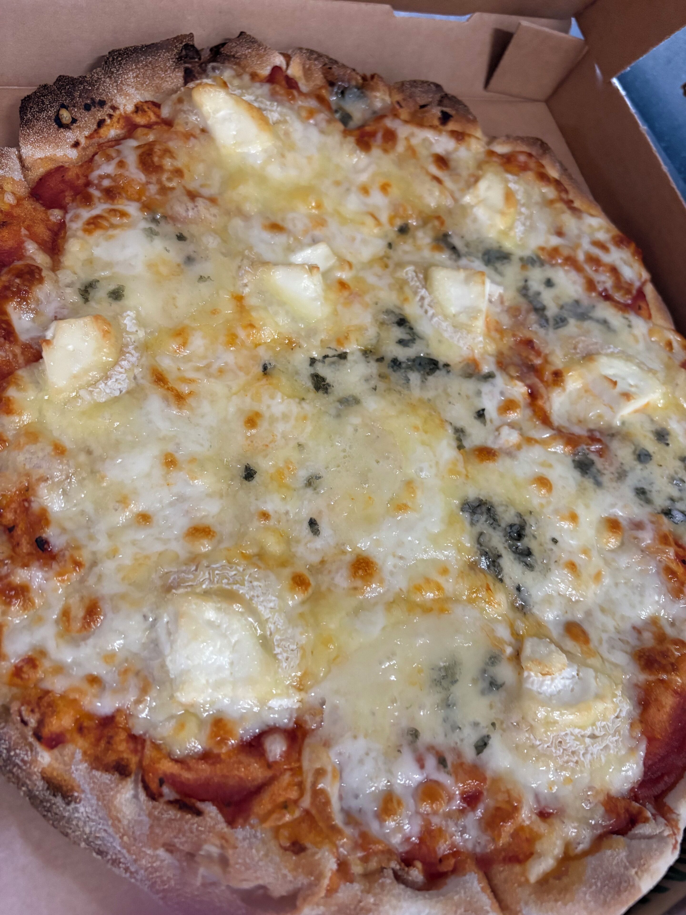 A pizza with melted cheese and herbs in a cardboard box.