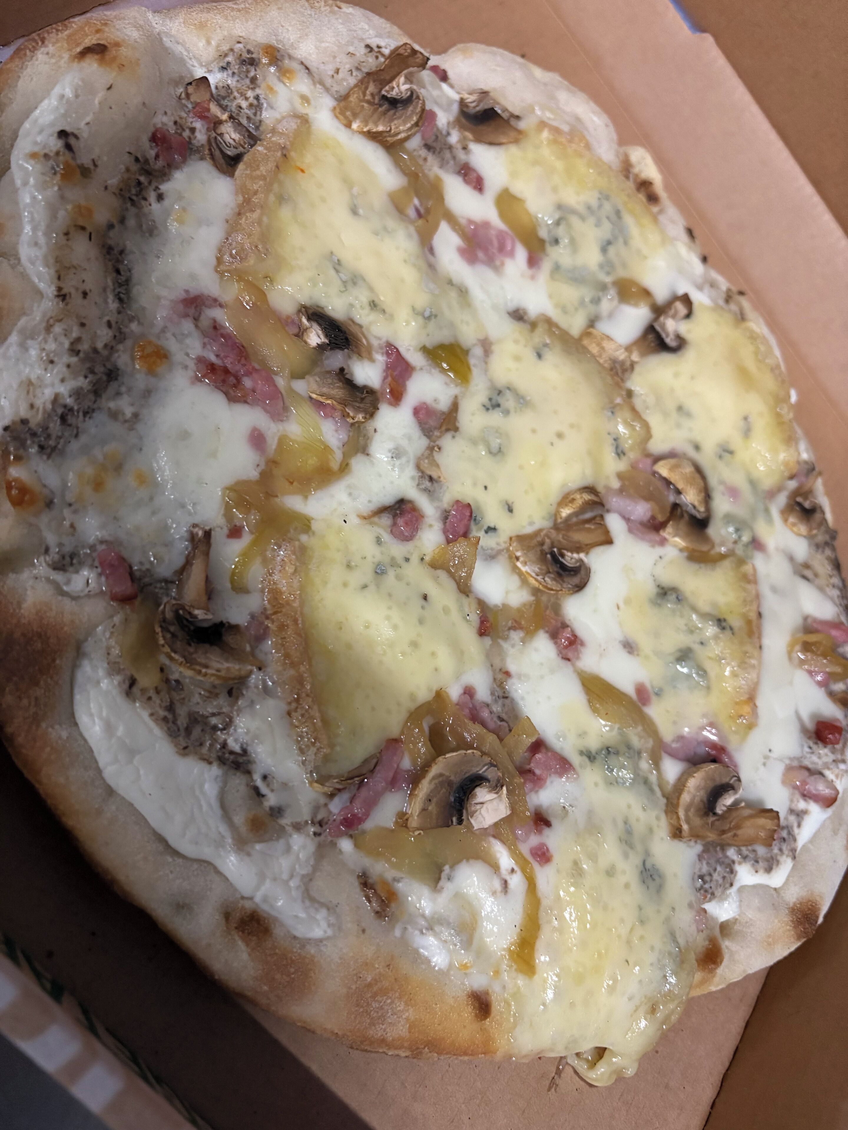 Pizza con queso, champiñones y jamón sobre un recipiente de cartón.