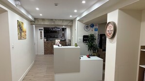 A hotel lobby with a reception desk, a bar, and a clock on the wall. - Comme chez soi (Jas)