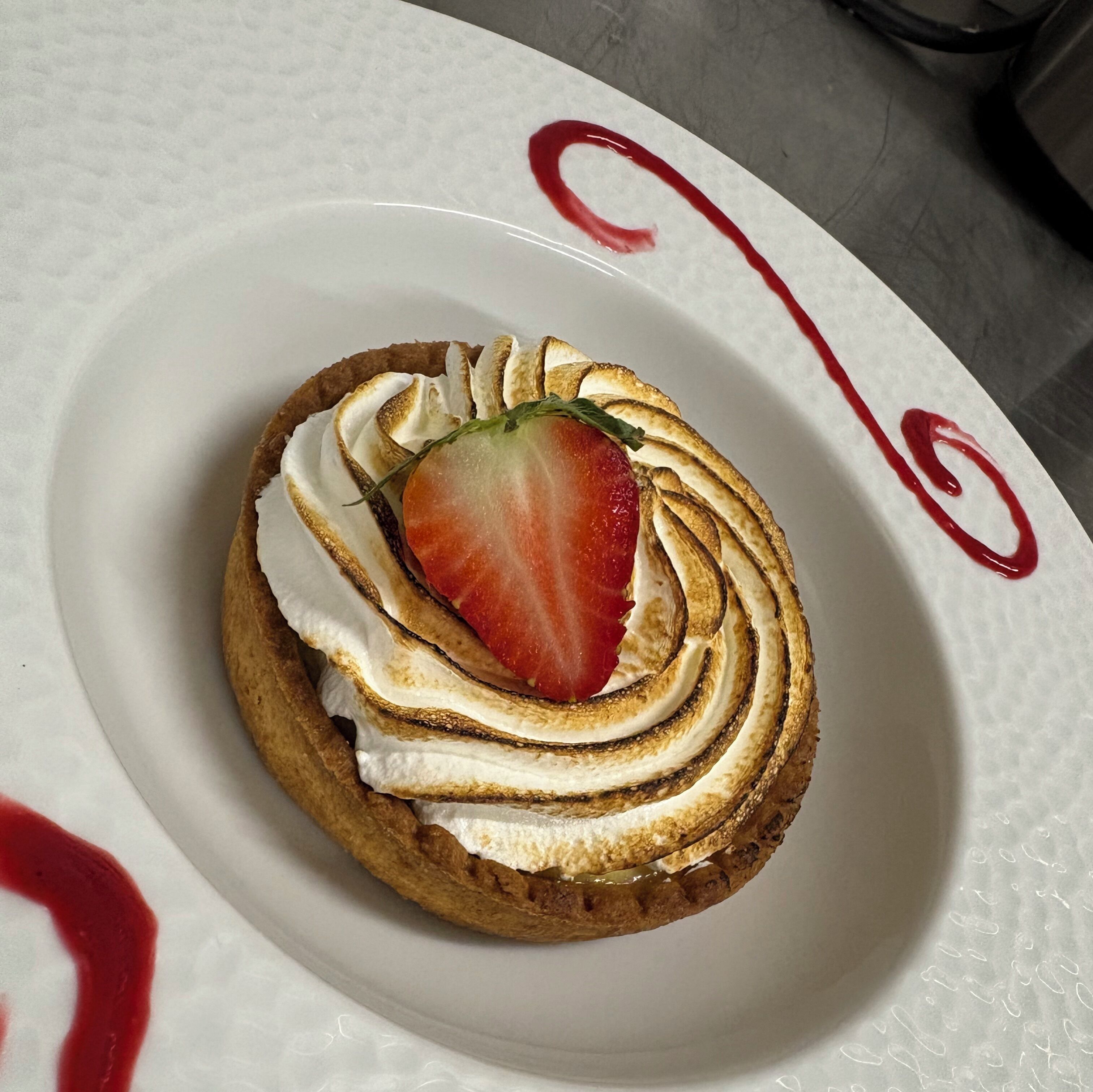 A dessert on a white plate with a decorative swirl and a strawberry on top.