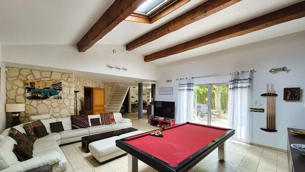 Un salón amplio con mesa de billar, un conjunto de sofás, una pared de piedra y una escalera que sube a otro nivel.
