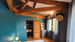 Un dormitorio con techo de madera, una cama con ropa de cama blanca, una estantería y una ventana con cortinas.