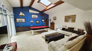 Un salón amplio con mesa de billar, sofá y mesa de futbolín.