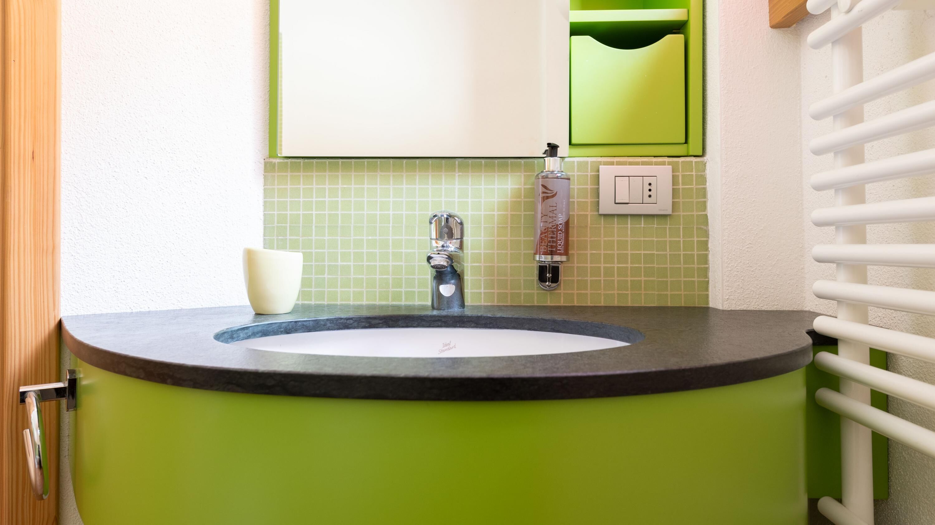 Une salle de bain avec un lavabo vert, un robinet blanc, un distributeur de savon et un miroir au-dessus du lavabo.