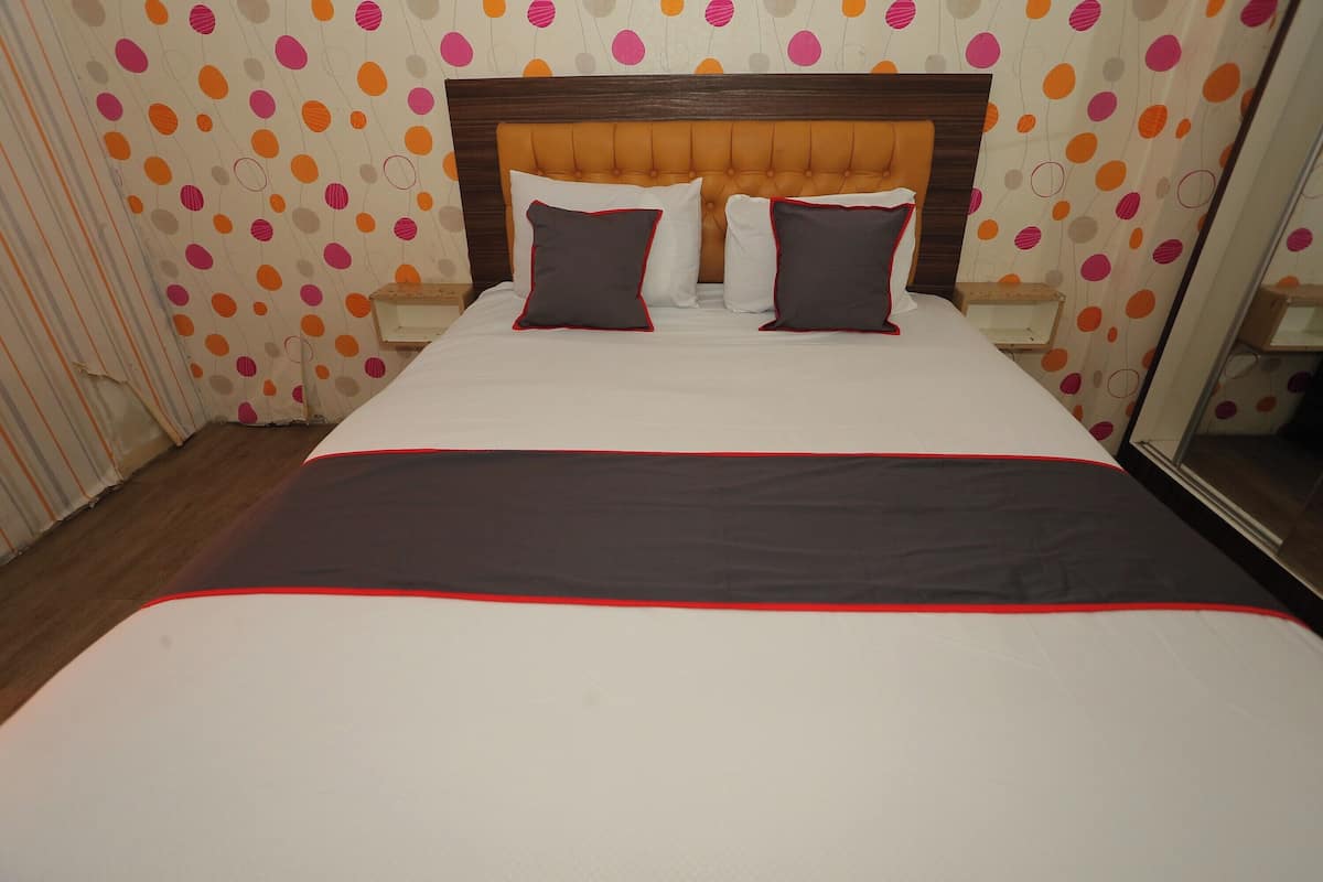 Ein Hotelzimmer mit einem großen Bett, zwei Kissen, einem Holz-Kopfteil und Tapete mit Punkten.