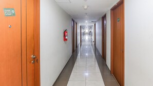 A long, narrow hotel corridor with wooden doors on either side, a fire extinguisher mounted on the wall, and a sign indicating the exit. - Capital O 93371 Pelangi Residence 5  (South Tangerang)