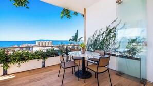 Un balcón con una mesa redonda y sillas, con vistas a una ciudad costera.