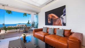 Ein modernes Wohnzimmer mit einem Ledersofa, einem Glastisch und einem großen Fenster mit Blick auf die Küste.