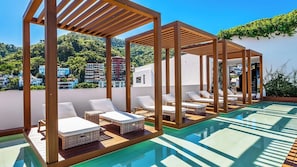 A rooftop swimming pool with wooden pergolas, lounge chairs, and a view of the cityscape.