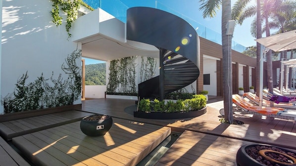 A modern outdoor area with a spiral staircase, wooden deck, and a seating area with a fire pit.