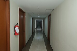 A long, narrow hallway with wooden doors on either side and a fire extinguisher mounted on the left wall.