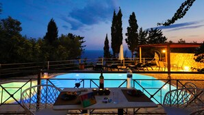 Un espace aménagé au bord de la piscine, avec une table dressée pour le dîner, une bouteille de vin et un verre d’eau.