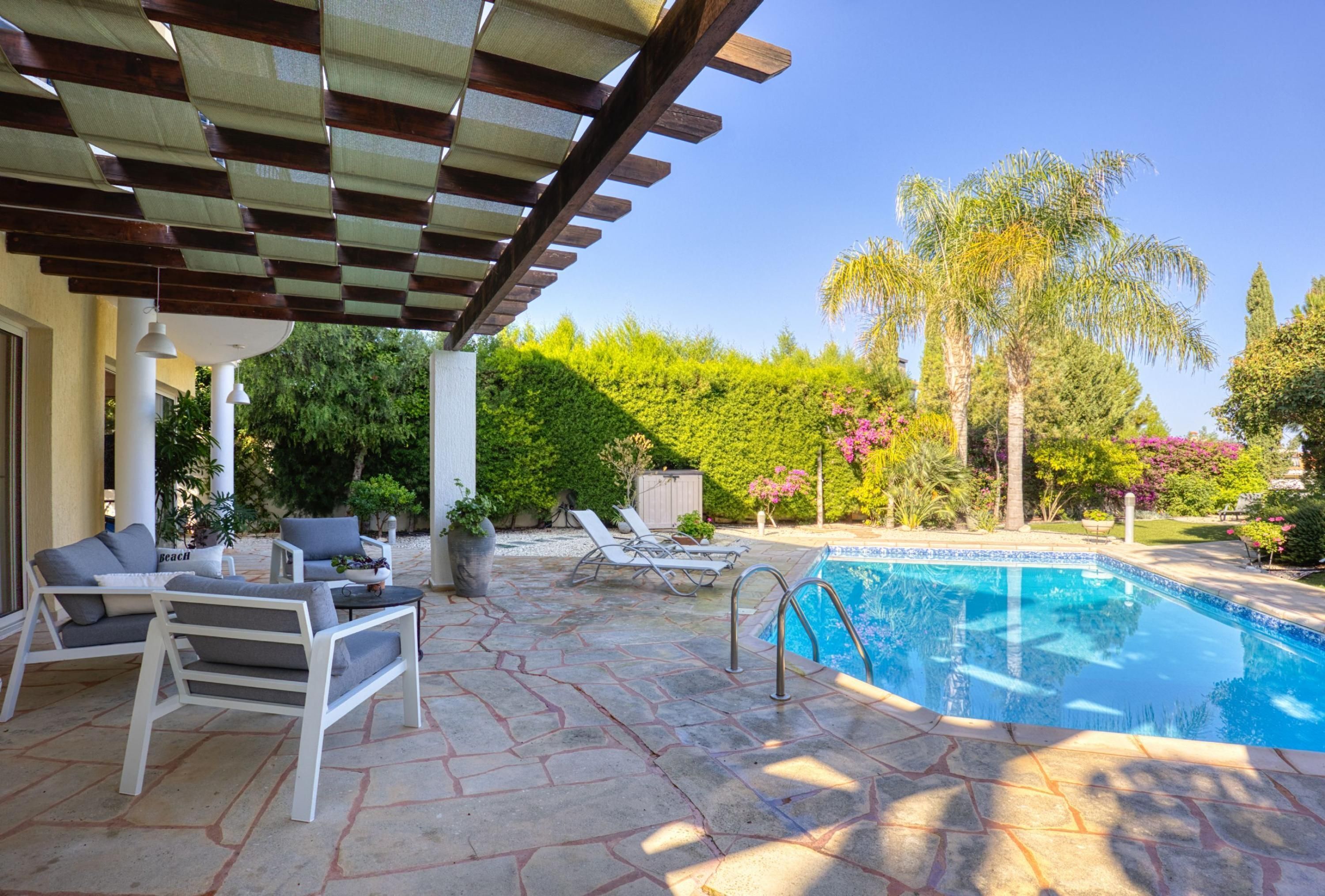 A covered outdoor area with a pool, lounge chairs, and a pergola.