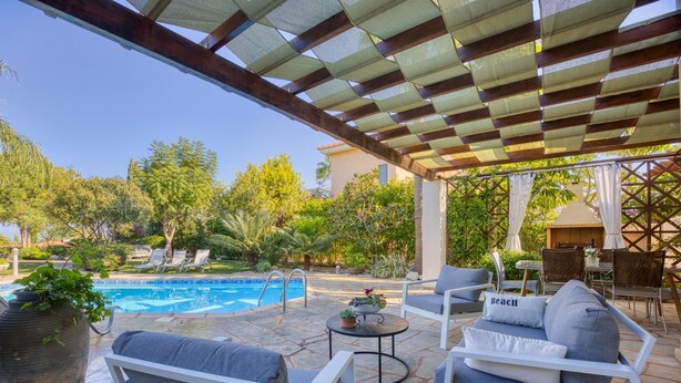 A poolside area with a covered patio, lounge chairs, and a dining table.