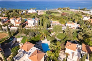 An aerial view of a residential area with houses, a swimming pool, and a view of the sea.