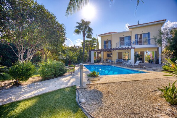 A two-story house with a swimming pool, surrounded by a well-maintained garden and palm trees.
