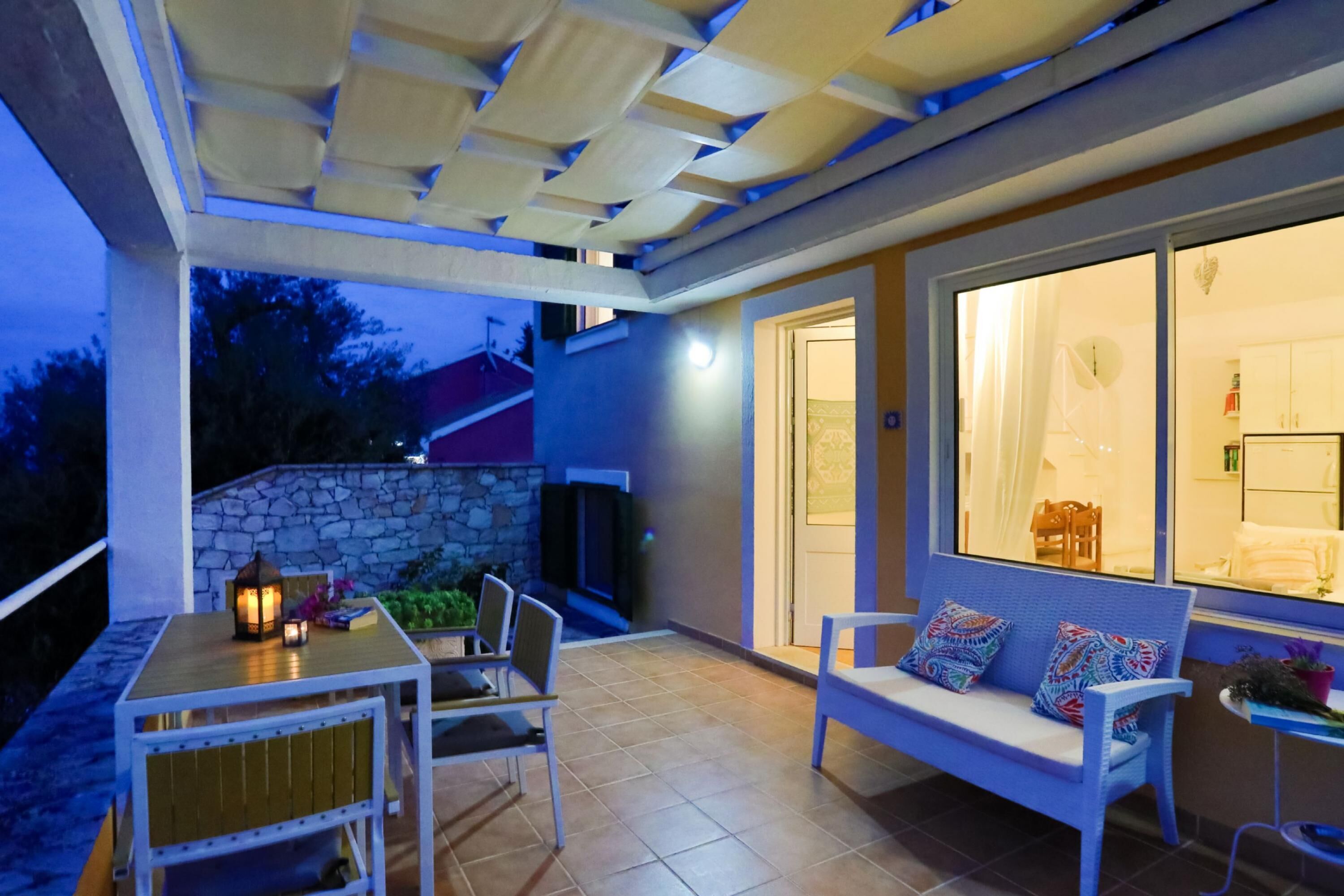 Un espace extérieur aménagé en terrasse, avec une table et des chaises, un banc avec des coussins et un mur en pierre.