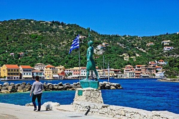 A coastal town with a statue, rocky shoreline, and colorful buildings.