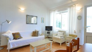Ein helles Wohnzimmer mit einer Couch, einem Fernseher, einem kleinen Tisch und einem Sessel.