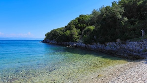 A clear coastal beach with rocky terrain and dense greenery. - Beach House Sophia in Paxi (Paxos)