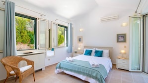 A bedroom with a bed, a chair, a nightstand, and a window with curtains. - Beach House Sophia in Paxi (Paxos)