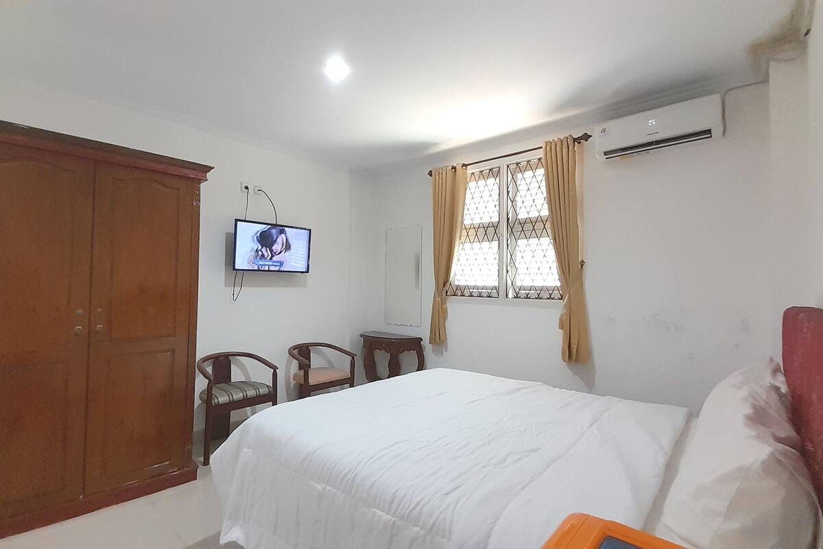 Une chambre à coucher comprenant un lit, un téléviseur fixé au mur, une fenêtre avec des rideaux et un appareil de climatisation.