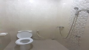 Une petite salle de bain carrelée, équipée de toilettes et d’une douche.
