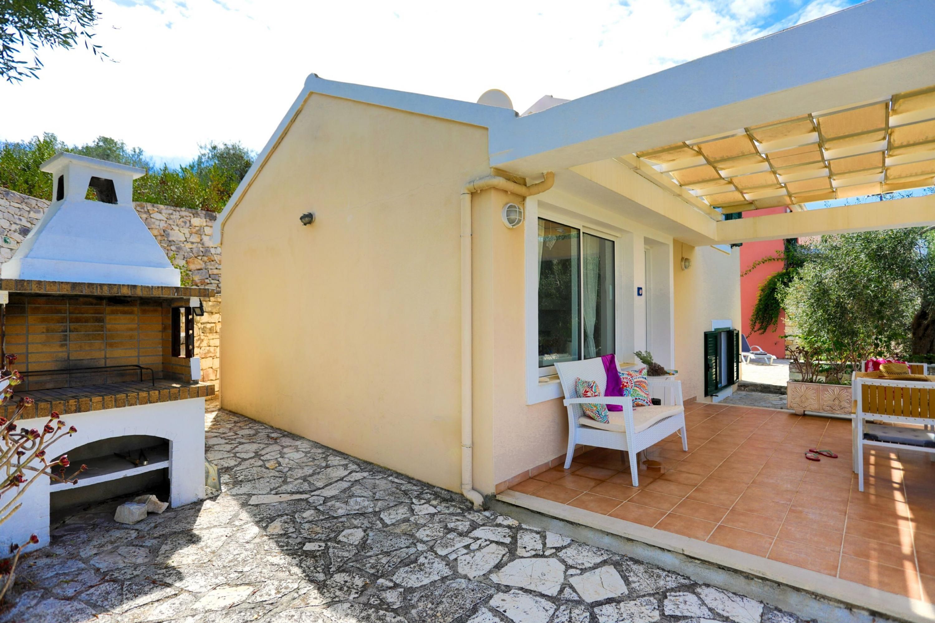 A patio area with a stone floor, a barbecue grill, a covered seating area, and a view of the surrounding landscape.