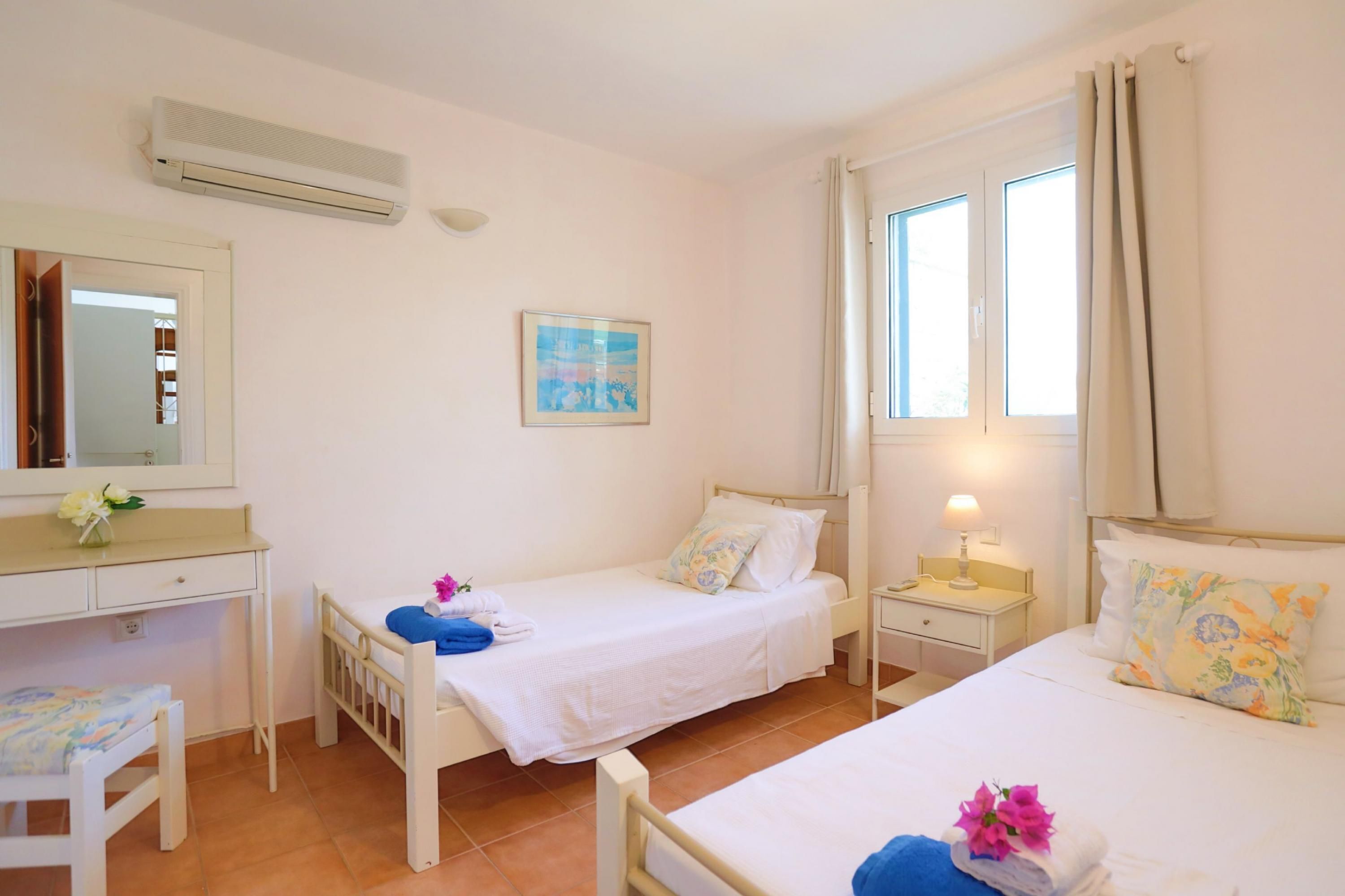 A room with two beds, a desk, a chair, a mirror, and a window with curtains.