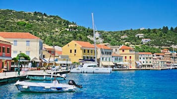 Un pueblo costero con edificios coloridos, un puerto deportivo con barcos y una colina al fondo.