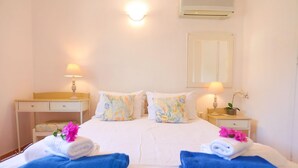 A hotel room with a bed, two bedside tables, a nightstand, a wall-mounted air conditioner, and a mirror. - Villa Stelios in Paxi (Paxos)