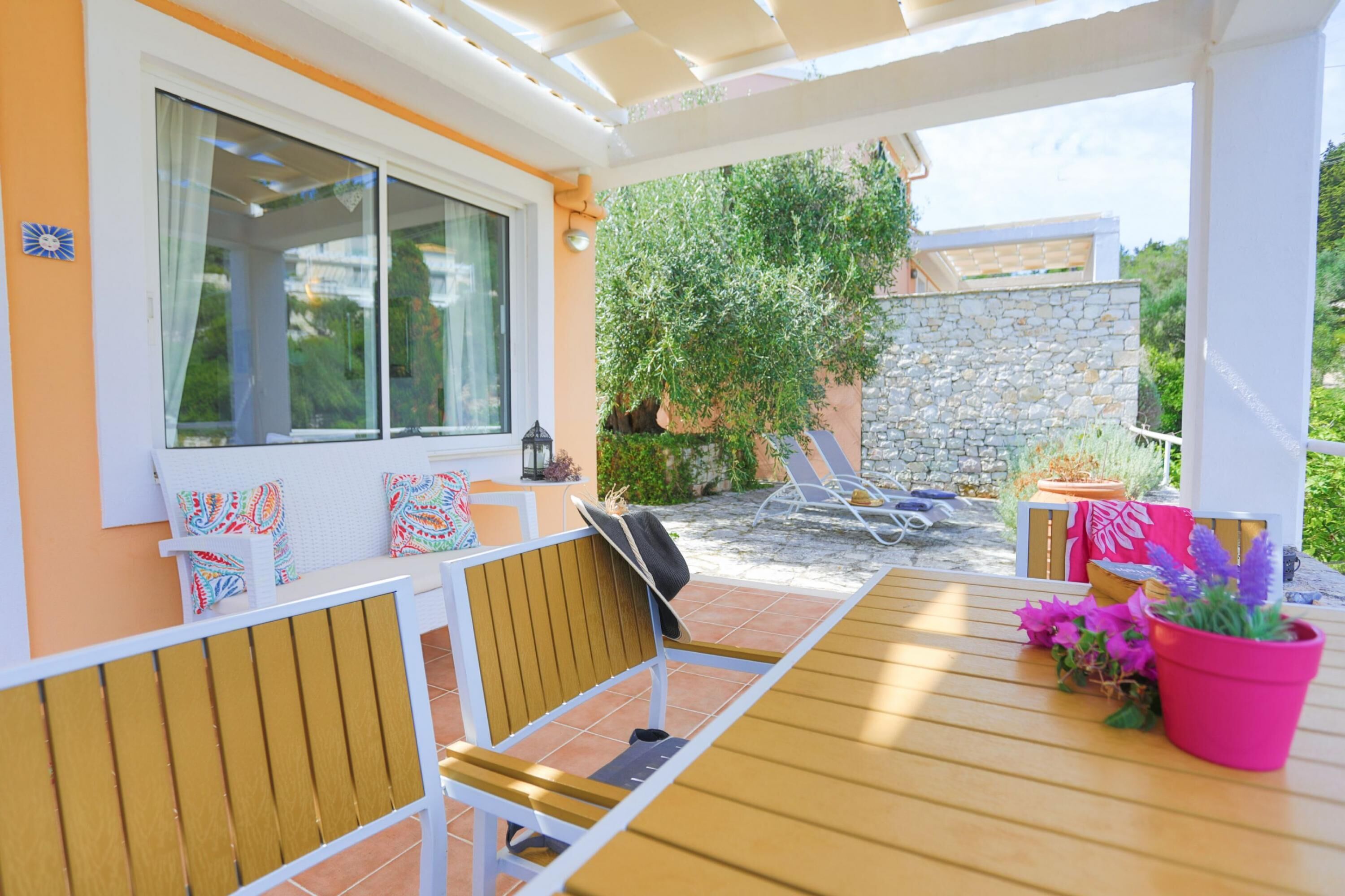 An outdoor patio with a wooden table and chairs, a stone wall, and potted plants.