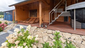 Un edificio moderno de madera con un espacio exterior cubierto, escalones de piedra y un muro de piedra con flores.