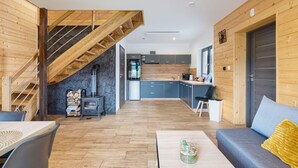 Un interior moderno con una escalera de madera, una chimenea de piedra, una cocina con armarios grises y una zona de estar con sofá y mesa de centro.