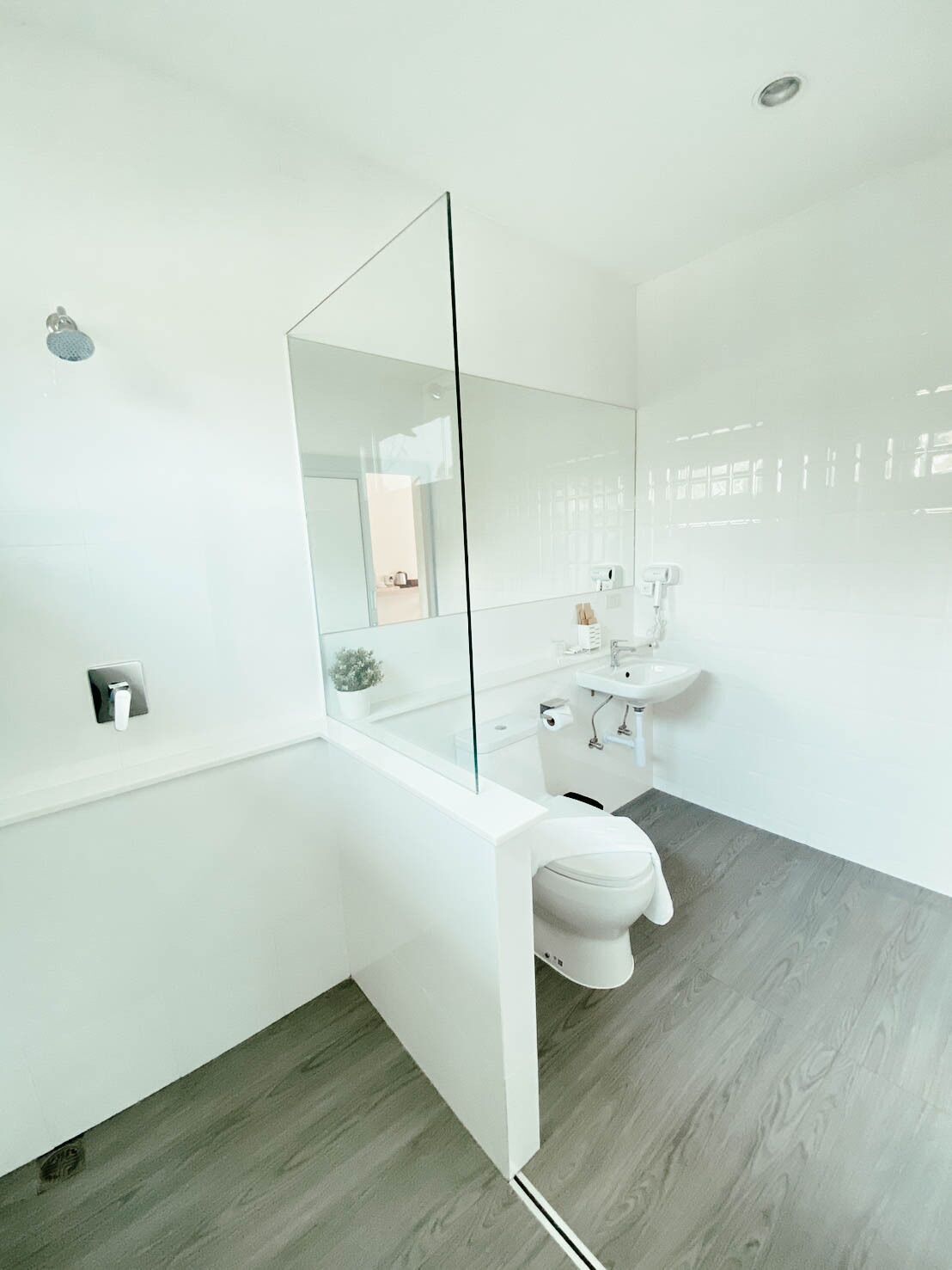 A modern bathroom with a glass partition, a toilet, a sink, and a shower.