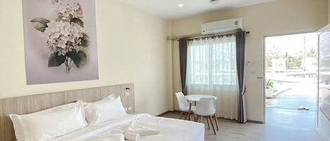A hotel room with a large bed, a small table with chairs, an air conditioning unit, and a view of the outdoors.