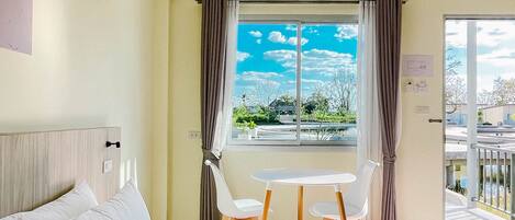 A hotel room with a bed, a small table with chairs, a window with curtains, and an air conditioning unit.