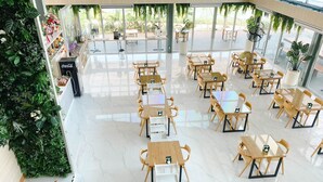 A spacious indoor area with multiple wooden tables and chairs, large windows, and indoor plants. - at Pream and Chan resort (Buriram)